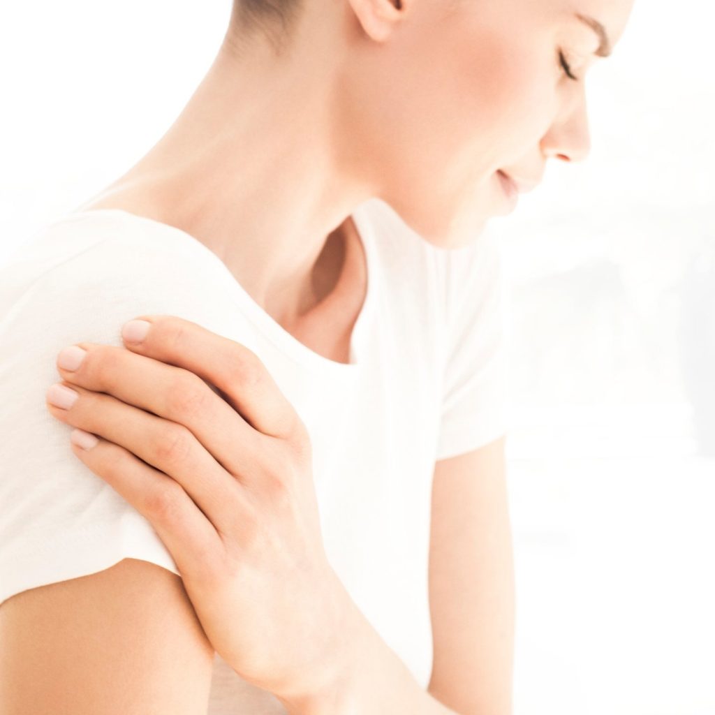 Woman in white shirt holding shoulder because of osteoarthritis and joint pain