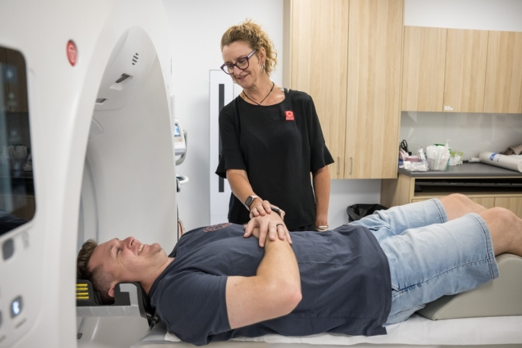 Radiographer support male patient as he enters CT scan.