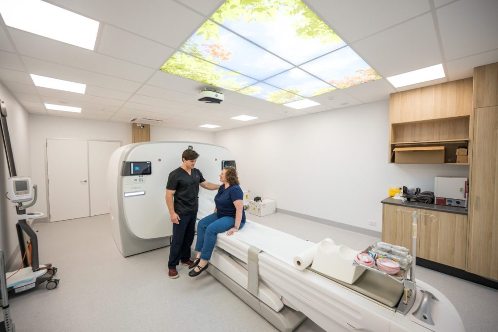 Sunshine Coast Radiology Nuclear Medicine Technician helps patient onto PET CT scanner bed